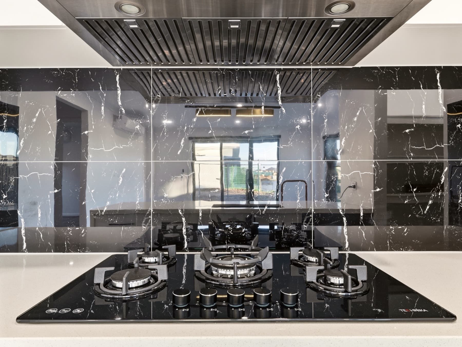 The five burner cooktop set into the bench against the veined splashback