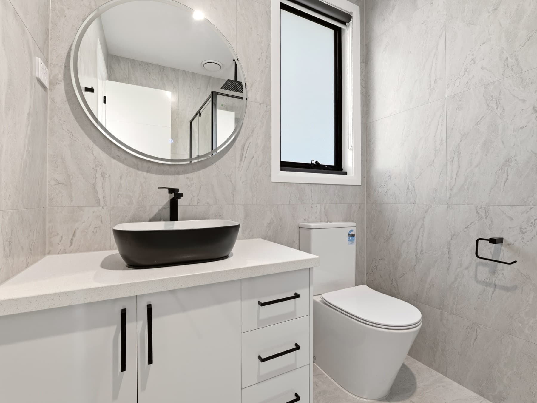 A bathroom vanity with round mirror and black basin