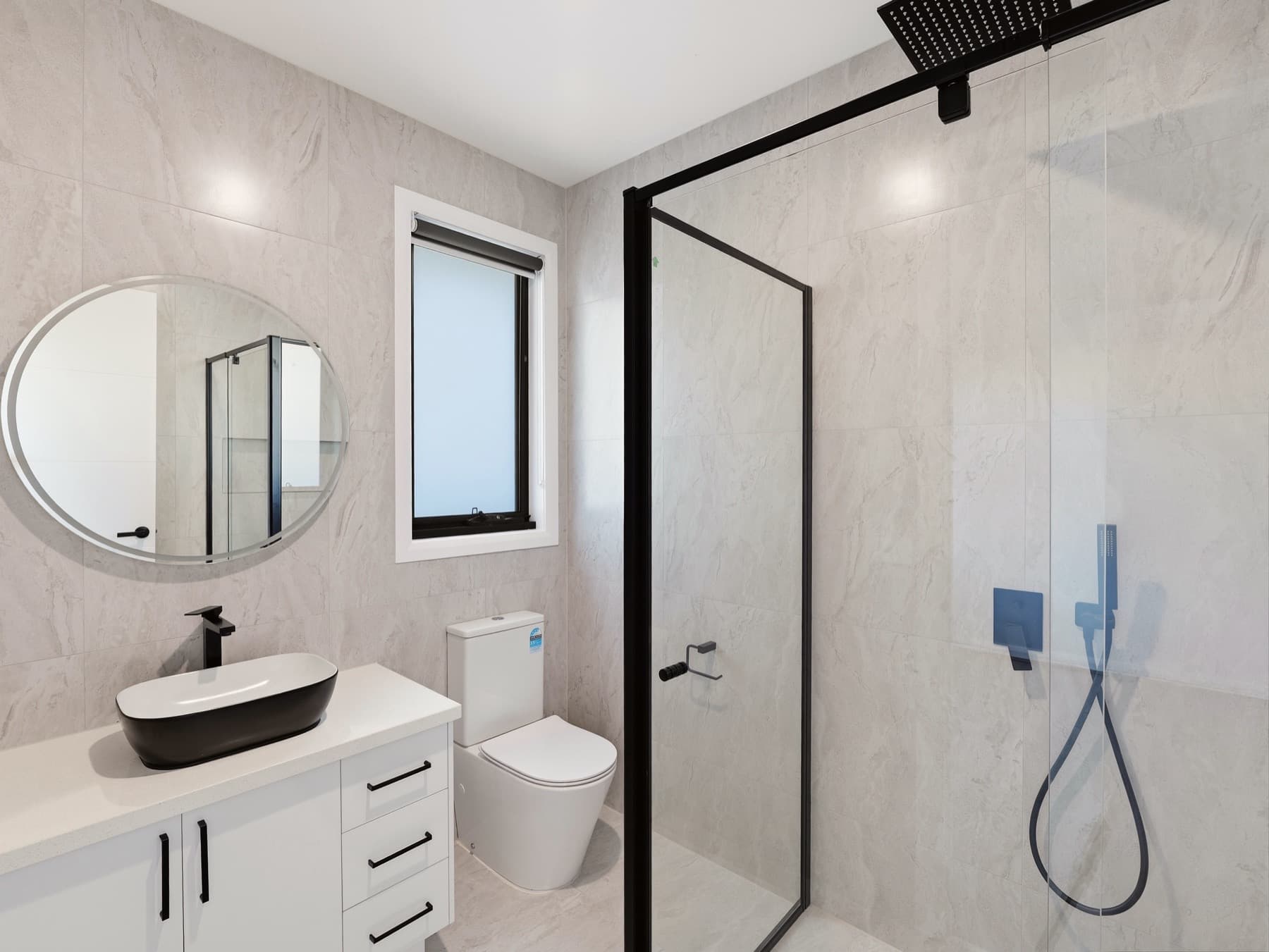 A bathroom with framed shower screen, round mirror and black basin