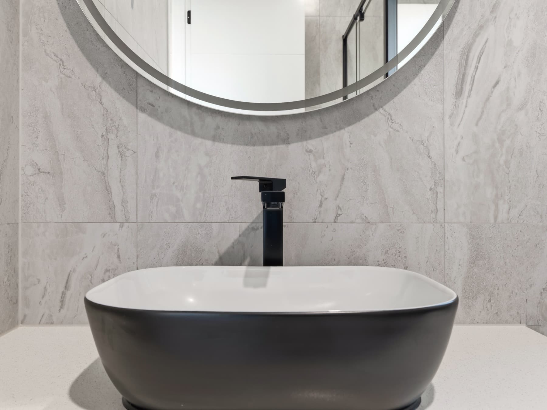 The black vessel basin beneath a round mirror, stone tiled wall behind